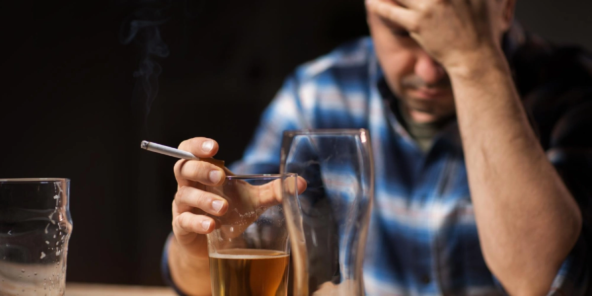 mężczyzna pije alkohol i pali papierosa (czynniki, które zwiększają możliwość wystąpienia hemoroidów)
