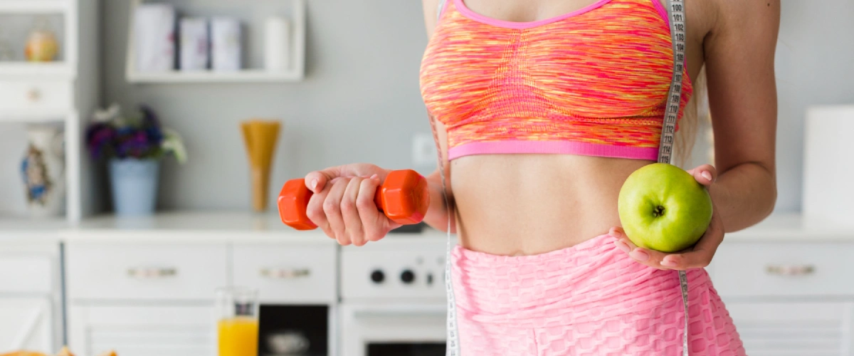 Wysportowana kobieta w kuchni trzyma hantel i jabłko