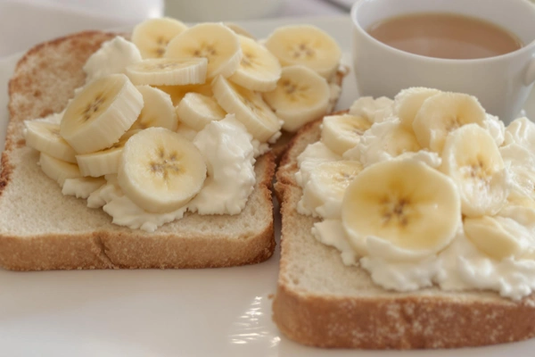 Dwie kromki pieczywa pszennego z chudym twarogiem i plastrami banana