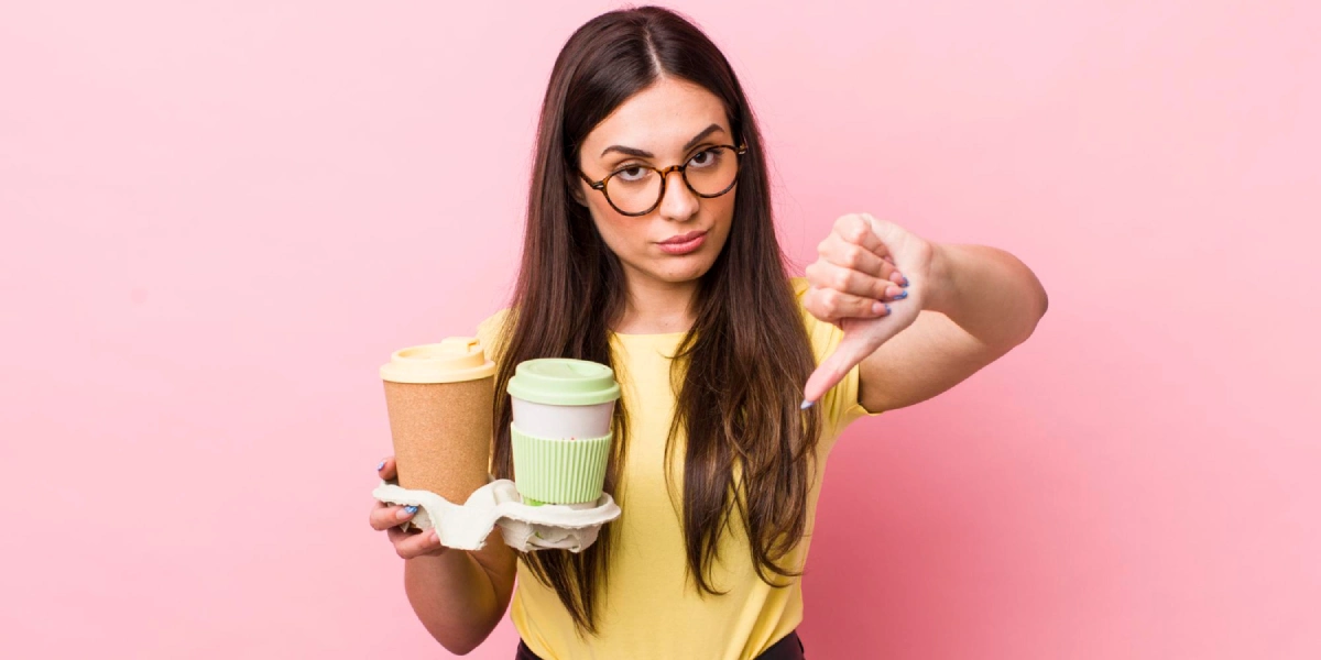 kobieta pokazuje kciuk w dół, trzymając w drugiej ręce kawę