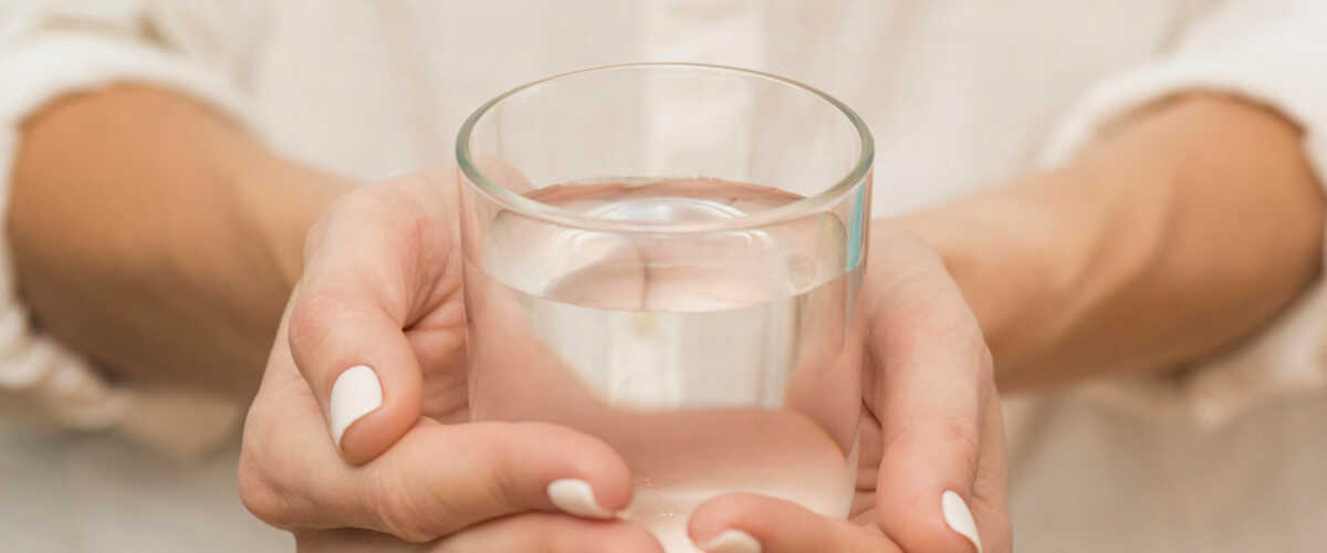dłonie ze szklanką wody - ile wody pić