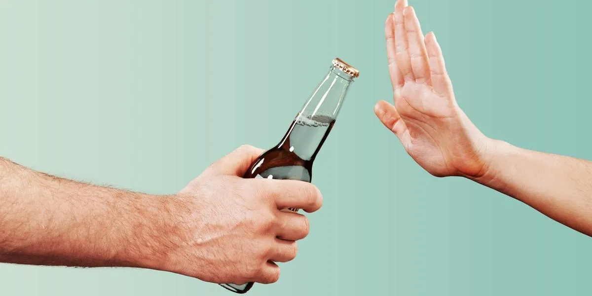Jedna osoba podaje butelkę z alkoholem, a druga odmawia jej przyjęcia gestem 