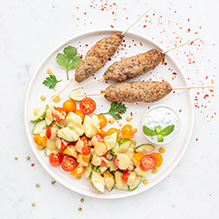 kolacja w diecie pudełkowej bez glutenu i nabiału - kofta wołowa z miętową raitą, sałatka z pomidorków koktajlowych i ogórka z sosem sezamowym